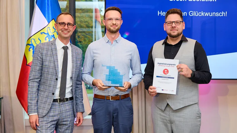 Digitalisierungsminister Dirk Schrödter steht mit zwei Vertretern von PROGEEK vor einer Leinwand mit der Aufschrift „Green Ecolution, Herzlichen Glückwunsch!“, einer hält die gläserne Trophäe, der andere die Urkunde
