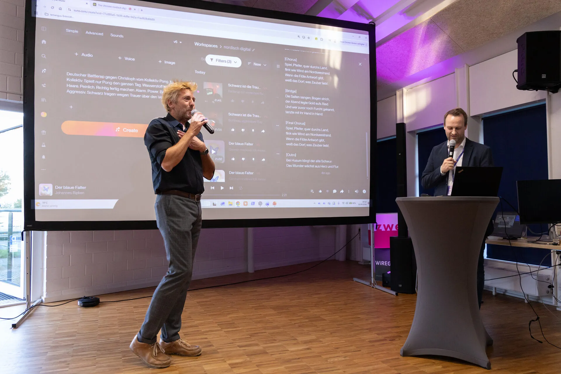 Johannes und Christoph beim KI Music Battle im Saal der lisezwei, auf der Leinwand der Prompt für den KI-Musikgenerator